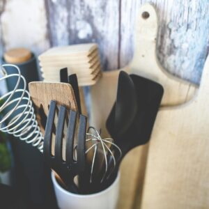 Collection of kitchen utensils including spatula, whisk, and chopping boards against a rustic background.