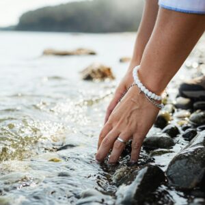 Hands gently touching water on a rocky shore with distant hills in view.