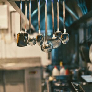 Stainless steel kitchen utensils hanging in a modern kitchen setting with blurred background.