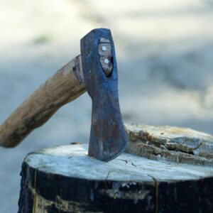 Close-up of a rusty axe head embedded in a chopped wooden log outdoors.