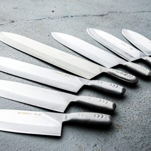 A variety of stainless steel knives neatly arranged on a textured concrete surface, showcasing sharpness and craftsmanship.