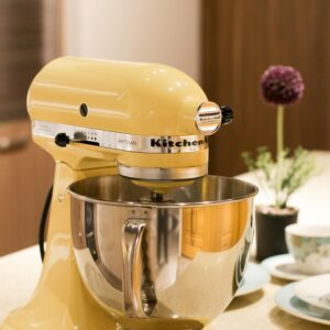 Vibrant yellow stand mixer on a kitchen countertop beside tableware and decor.