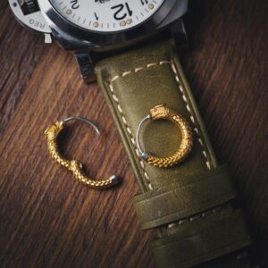 Elegant wristwatch with gold snake earrings on a leather strap, showcasing luxury details.