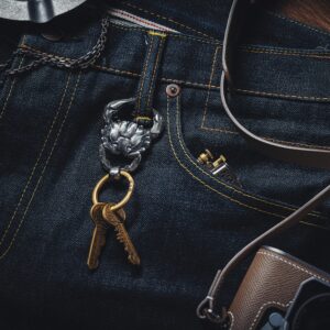 Close-up of a silver crab keychain attached to jeans, next to a vintage camera.