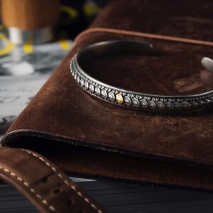 Close-up of a silver bracelet with intricate design, resting on a leather wallet.