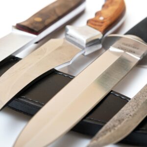 Close-up of different knives with diverse handles and blades on a black leather sheath.