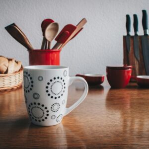 A cozy kitchen scene featuring a decorative mug, cutlery set, and fresh bread basket on a wooden table.