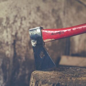 Detailed view of a red handled axe embedded in a wooden stump, outdoors.
