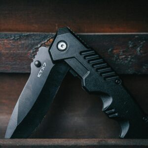 Close-up of a black folding knife on a wooden background, emphasizing its sharp blade.