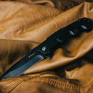 A sleek black folding knife on a textured brown leather surface, showcasing its design.