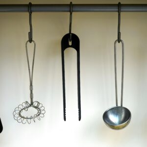 A set of stainless steel and plastic kitchen utensils hanging on a rail.