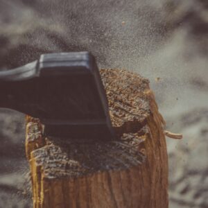 Close-up of an axe striking a wood log outdoors, creating dust and splinters.