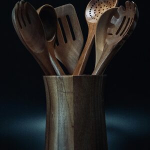 A collection of wooden kitchen utensils displayed in a stylish holder against a dark background.