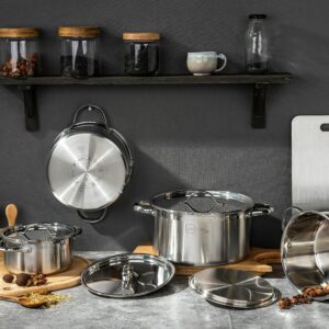 Stainless steel pots and kitchen essentials on concrete surface under shelf with jars.