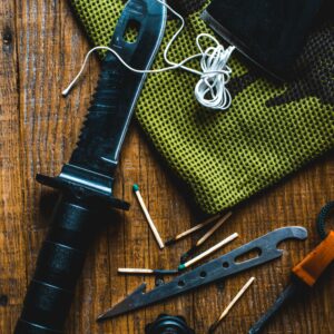 Flat lay of survival gear including a knife, matches, and compass for outdoor adventure.