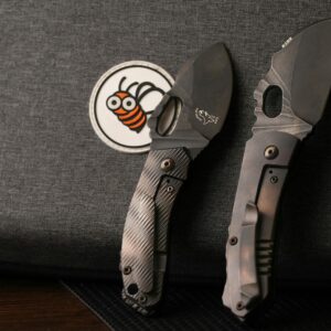 Two tactical knives resting on dark fabric with a bee patch, highlighting knife design details.