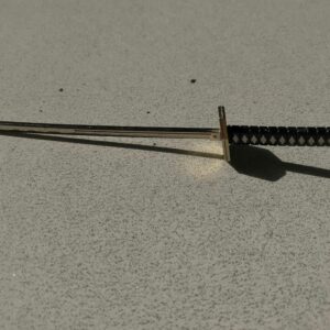 Close-up of a miniature katana sword keychain casting a shadow on a textured surface.
