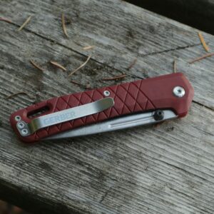Close-up of a red folding pocket knife on a wooden bench outdoors.