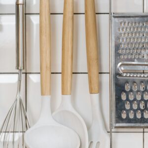 Aesthetic arrangement of kitchen utensils including a whisk, ladle, spatula, and grater on a tiled wall.