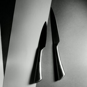 Artistic black and white photo of stainless steel knives on a geometric paper design.