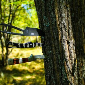 Close-up of three knives embedded in a tree trunk in a sunlit forest setting.